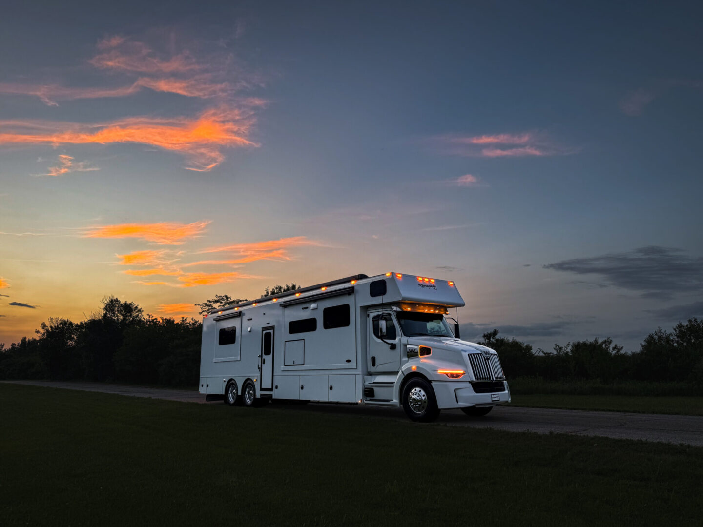 White RV parked at sunset on road.