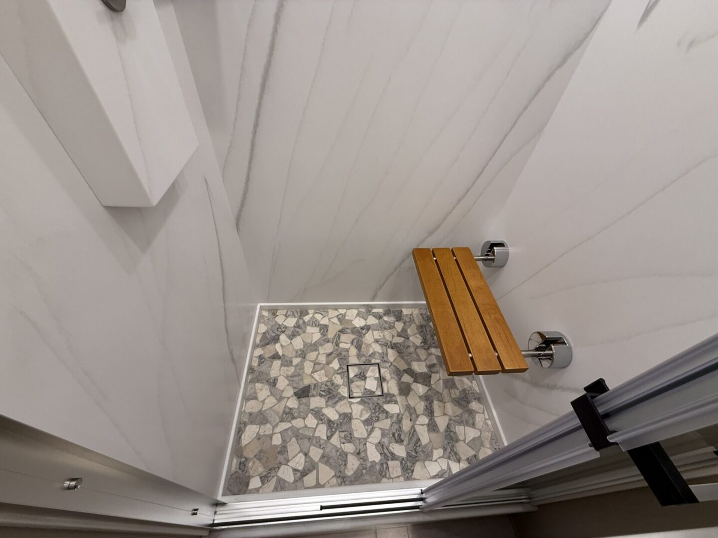Modern shower with wooden bench and mosaic tile.
