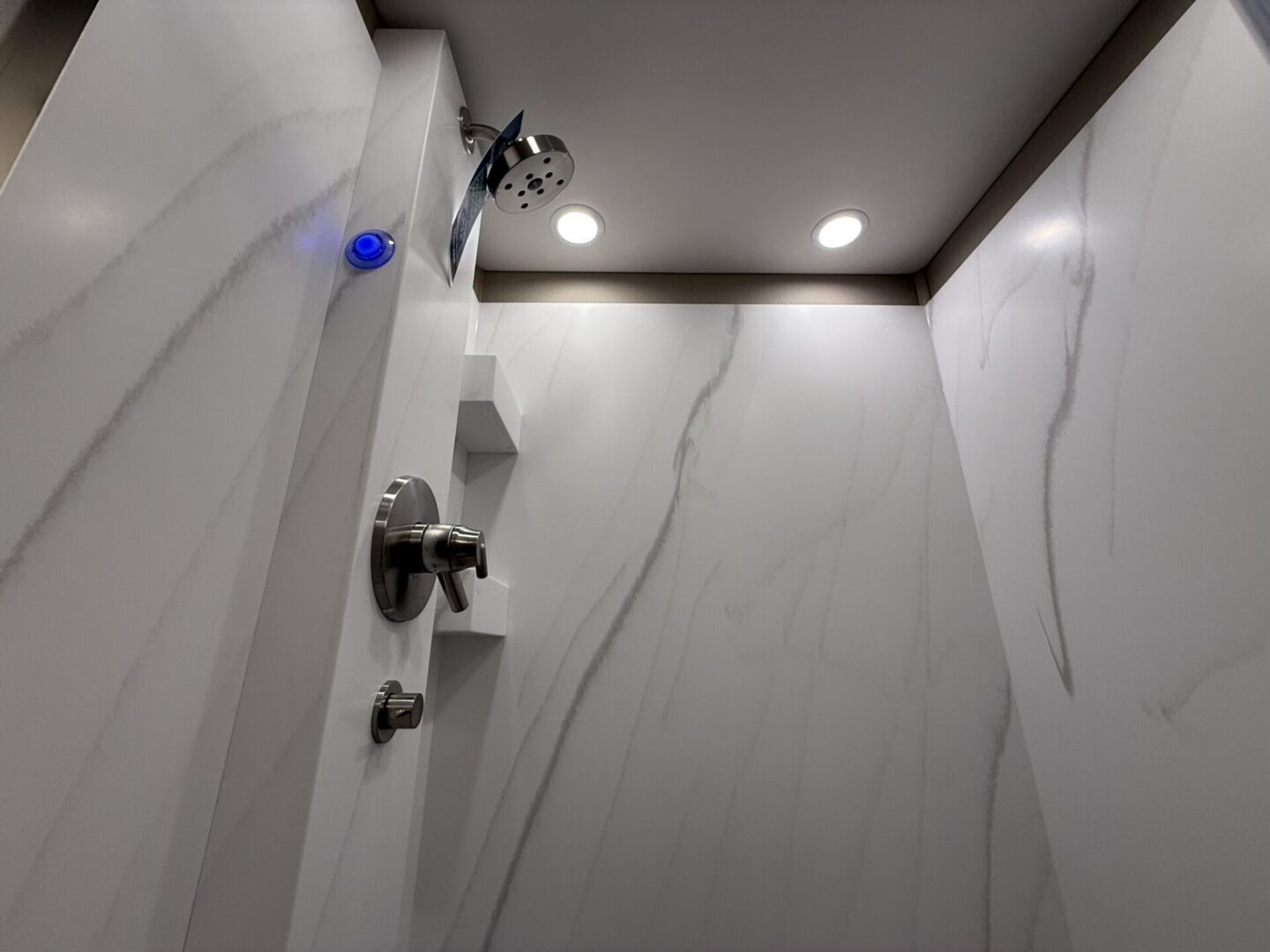 Modern shower with marble walls and lighting.